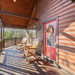 Front porch with two rocking chairs, round-log siding and a red front door with a wreath