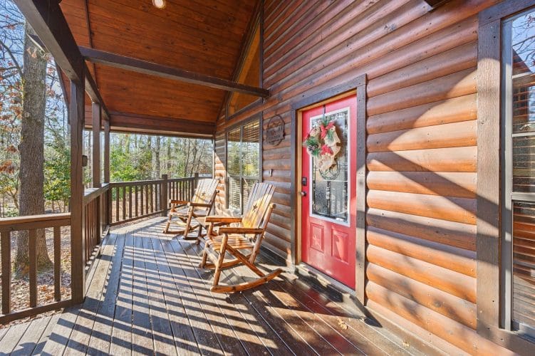 Front porch with two rocking chairs, round-log siding and a red front door with a wreath