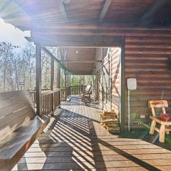 Long covered porch with a built-in bench, a wooden chair and stacked firewood