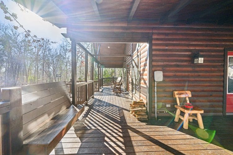 Long covered porch with a built-in bench, a wooden chair and stacked firewood