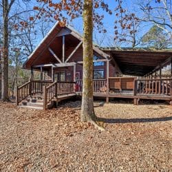 Cabin from the yard with the covered porch and deck to one side, in winter woods