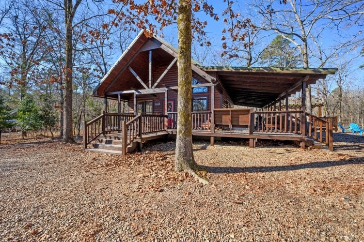 Cabin from the yard with the covered porch and deck to one side, in winter woods