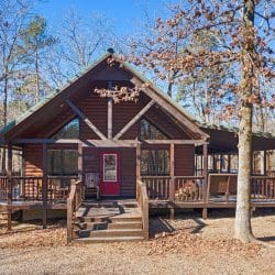 Front of the cabin with an A-frame gable of windows, red door and deck