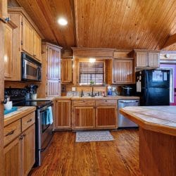 Kitchen with wood cabinets, tile counters, black refrigerator and stove, and a window over the sink