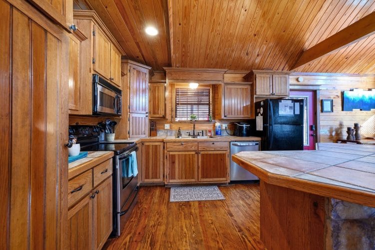 Kitchen with wood cabinets, tile counters, black refrigerator and stove, and a window over the sink