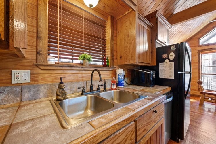 Double sink with tile countertop and a black refrigerator