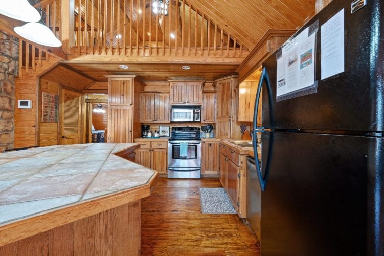 Kitchen with a tile-topped island, stainless range and microwave, and the loft railing overhead