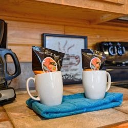 Coffee maker with two white mugs on a teal towel beside the stove