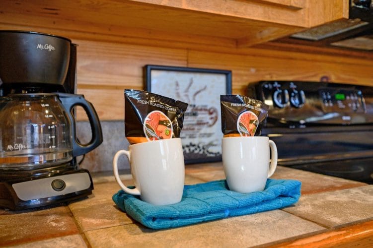 Coffee maker with two white mugs on a teal towel beside the stove