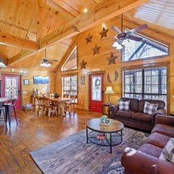 Open main room with a pitched pine ceiling, brown sofas, a round coffee table, and the dining area and kitchen behind