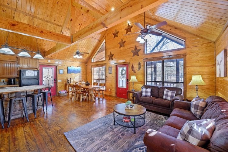 Open main room with a pitched pine ceiling, brown sofas, a round coffee table, and the dining area and kitchen behind