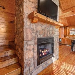 Stone fireplace with a gas fire burning and a TV mounted above it, with steps up beside it