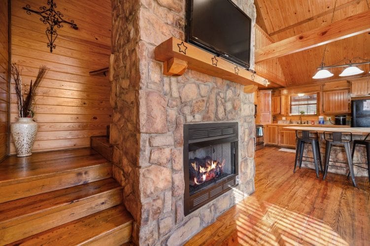 Stone fireplace with a gas fire burning and a TV mounted above it, with steps up beside it