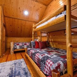 Upstairs sleeping area with a log twin-over-queen bunk bed and another bed under red-and-gray plaid quilts
