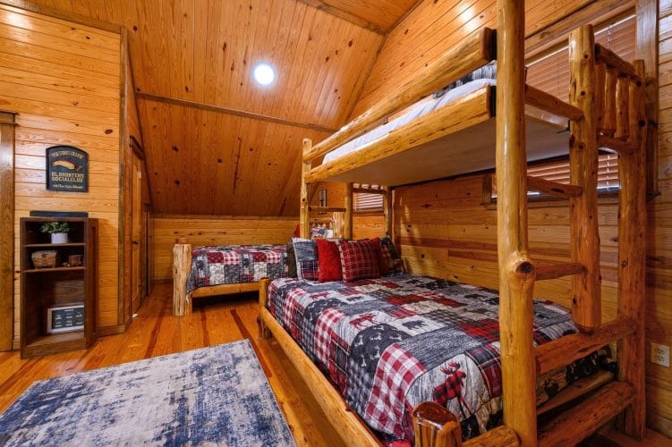 Upstairs sleeping area with a log twin-over-queen bunk bed and another bed under red-and-gray plaid quilts