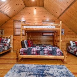 Upstairs sleeping area with a log twin-over-queen bunk in the middle and a bed on each side