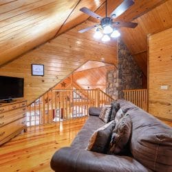 Upstairs sitting area with a leather sofa, a TV on a dresser and the stair railing beside it