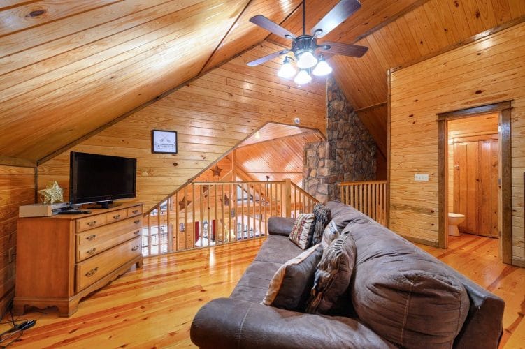 Upstairs sitting area with a leather sofa, a TV on a dresser and the stair railing beside it