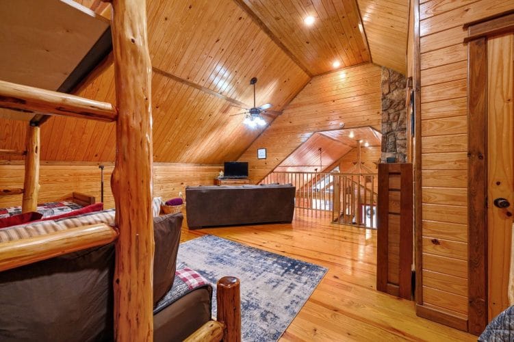 Upstairs room looking toward the stairs, with a sofa and a log bed frame in the foreground