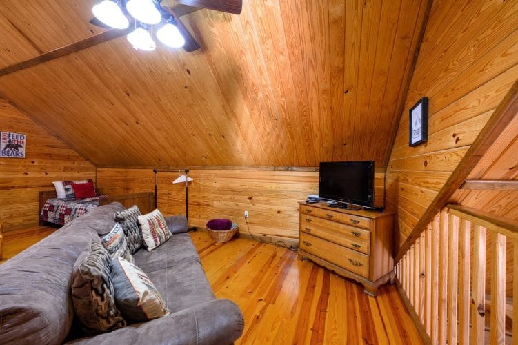Upstairs seating with a sofa and a TV on a dresser, and bunks and a bed along the far wall