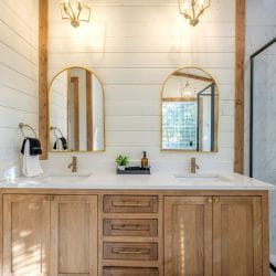 Double vanity with arched gold mirrors and a glass shower