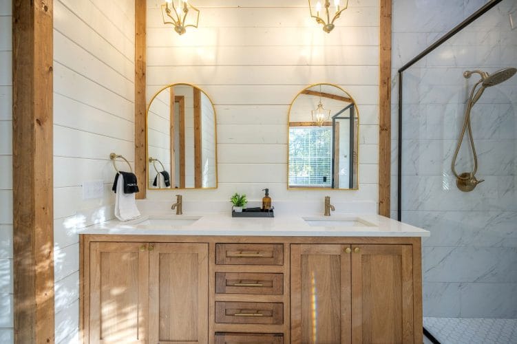 Double vanity with arched gold mirrors and a glass shower