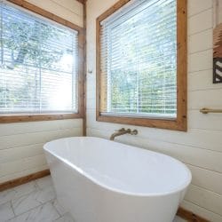 Freestanding tub under two windows beside mountain-pattern wall art