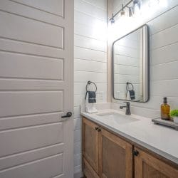 Wood vanity with a black-framed mirror beside a white door