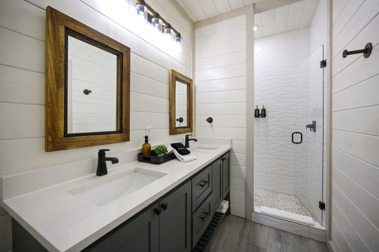Double vanity with wood-framed mirrors and a glass shower