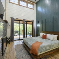 King bed with a dark green slat accent wall, sliding glass doors and a tiled fireplace at left