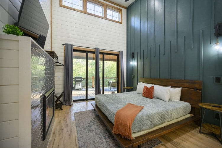 King bed with a dark green slat accent wall, sliding glass doors and a tiled fireplace at left