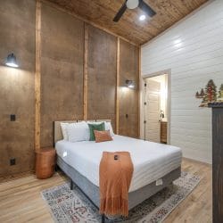 Bedroom with a brown paneled accent wall, a white bed, a dresser and a ceiling fan