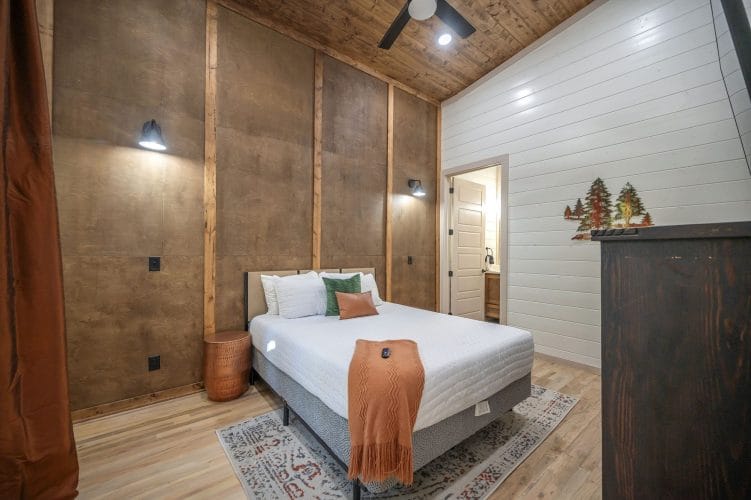 Bedroom with a brown paneled accent wall, a white bed, a dresser and a ceiling fan