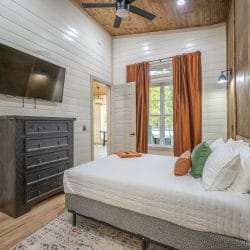 Same bedroom with a TV on the wall and orange curtains
