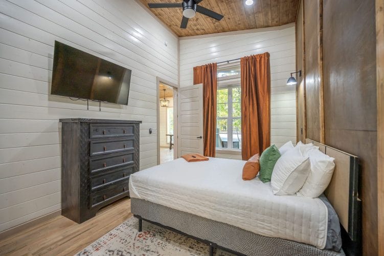Same bedroom with a TV on the wall and orange curtains