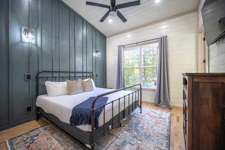 King black iron bed with a navy throw against a dark green board-and-batten wall
