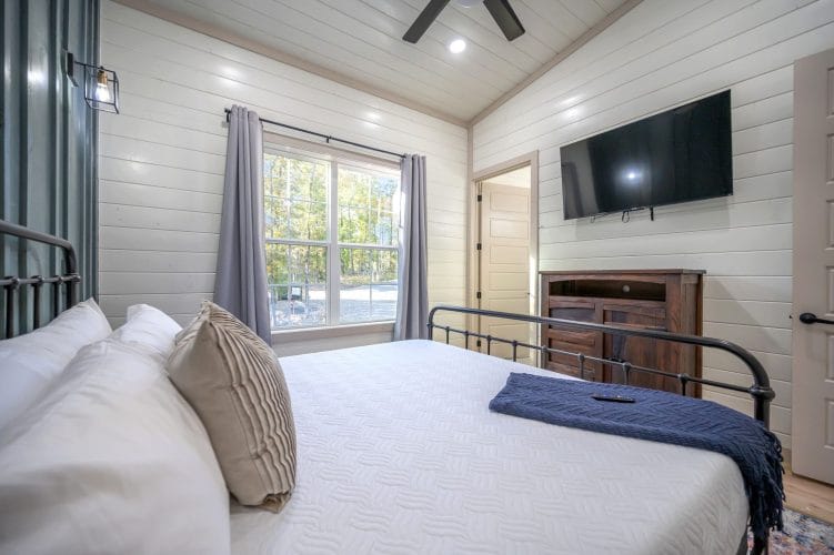 Same bedroom with a wall TV and a window with gray curtains