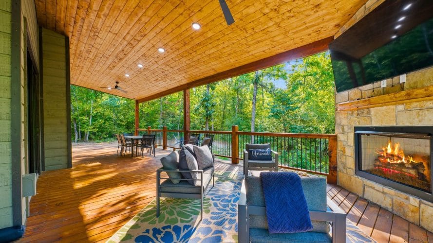 Covered deck with an outdoor sofa, a gas fireplace, a TV and a long table