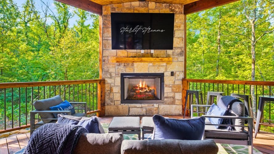 Stone fireplace with a TV above it and lounge furniture on the covered deck