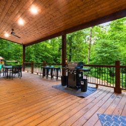Covered deck with a grill, a dining table and the playset in the trees