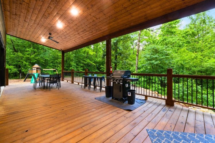 Covered deck with a grill, a dining table and the playset in the trees
