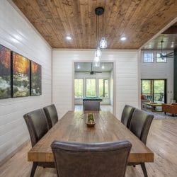 Long wood dining table with leather chairs and a framed forest triptych