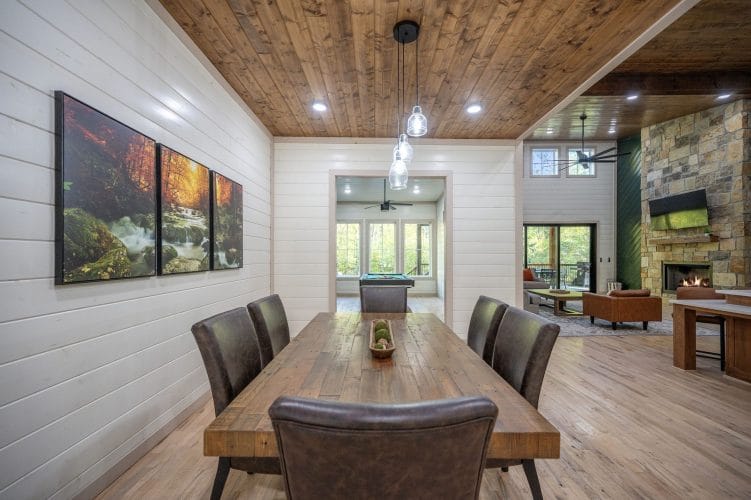 Long wood dining table with leather chairs and a framed forest triptych