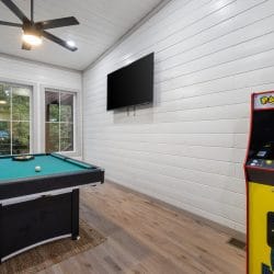 Game room with a green-felt pool table and a Pac-Man arcade cabinet under a wall TV