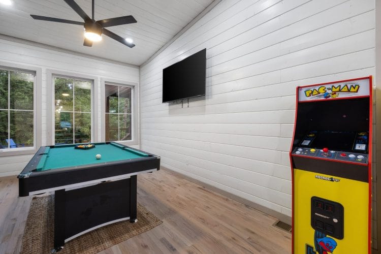 Game room with a green-felt pool table and a Pac-Man arcade cabinet under a wall TV