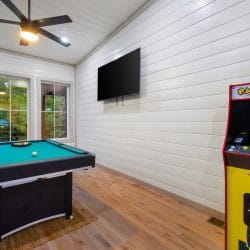 Pool table and Pac-Man cabinet by tall windows, with a wall TV
