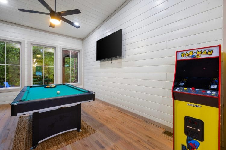 Pool table and Pac-Man cabinet by tall windows, with a wall TV