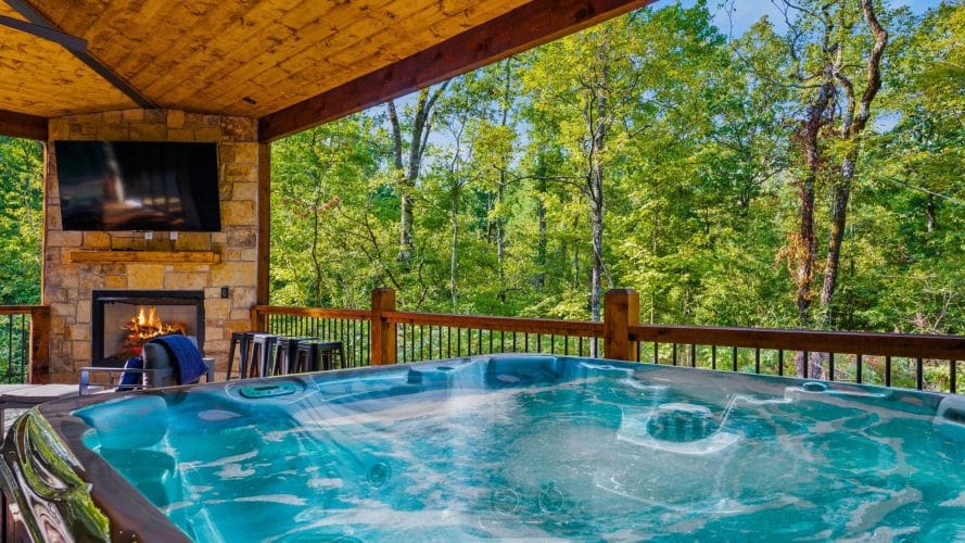 Hot tub on the covered deck with a stone fireplace and TV behind it