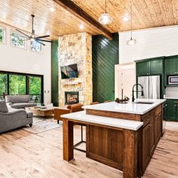 Kitchen with forest-green cabinets and a wood island, the stone fireplace in the great room beyond