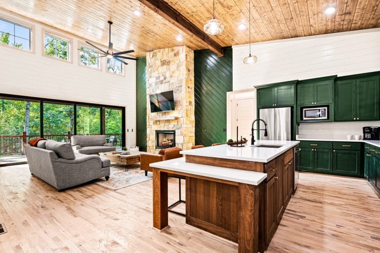 Kitchen with forest-green cabinets and a wood island, the stone fireplace in the great room beyond